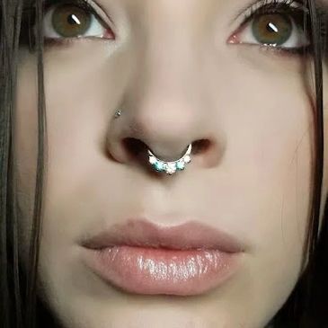 Close-up of a woman's face with septum and nose piercings.