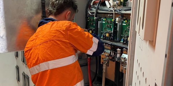 Electrician working on a large electrical panel with cables and tools.