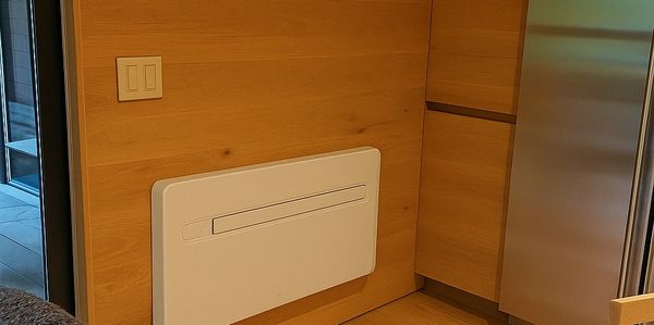 Modern kitchen corner with wooden panels, stainless steel fridge, and a white wall-mounted heater.