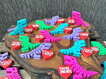 Colorful dinosaur magnets with red hearts saying cute dinosaur-themed compliments.