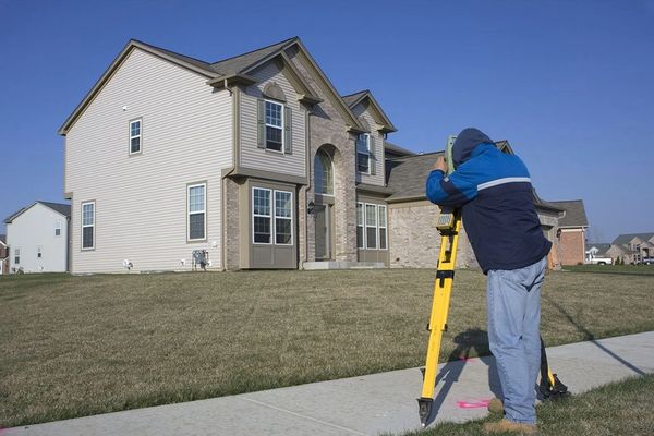 A land surveyor using equipment in front of a house.