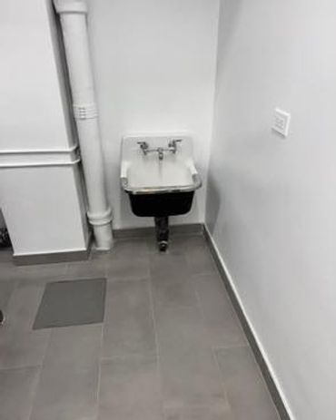 A small wall-mounted utility sink in a corner with gray tiled floor.