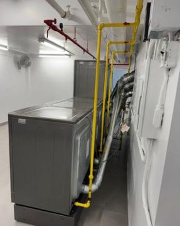 Industrial washing machines with yellow gas pipes in a clean laundry room.