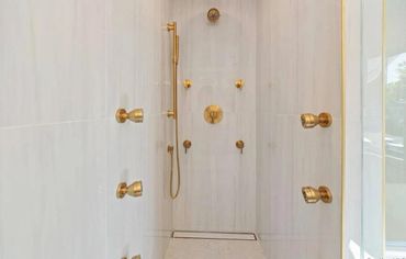 Luxurious shower with multiple gold showerheads and controls.