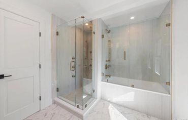 Modern bathroom with glass shower and bathtub, featuring marble floors.