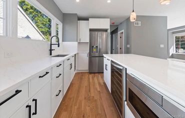 Modern kitchen with white cabinets, stainless steel appliances, and wooden floor.