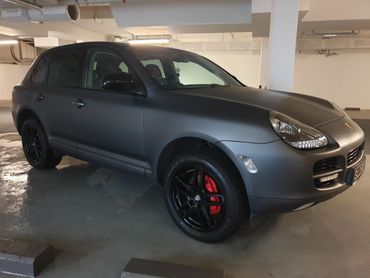 Matte black Porsche SUV parked in a dimly lit garage.