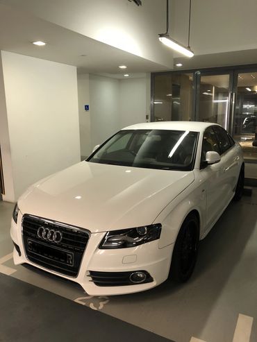 White Audi sedan parked in an indoor garage under bright lights.
