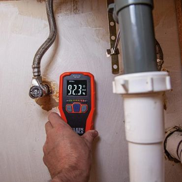 Hand holding moisture against the wall under a sink with 92.3% moisture readout
