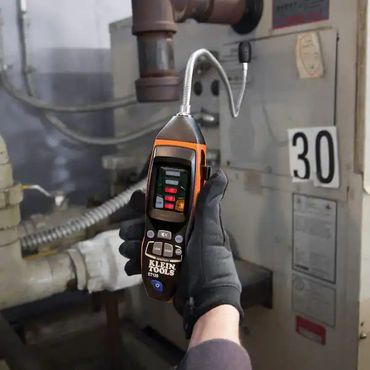 Gloved hand holding propane natural gas leak detector near a gas fired hvac unit