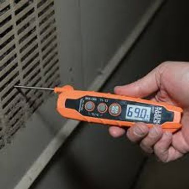 Hand holding orange probe thermometer checking return air grille of an A/C unit
