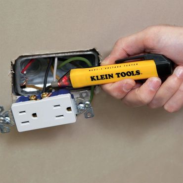 Hand holding a non-contact voltage tester checking an open electrical receptacle