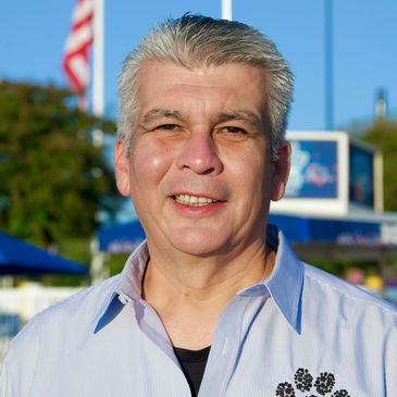 Smiling man wearing a Wounded Paw Project shirt outdoors on a sunny day.