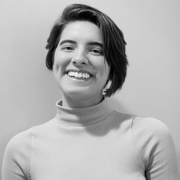 Young woman with short hair smiling warmly in a black and white portrait.