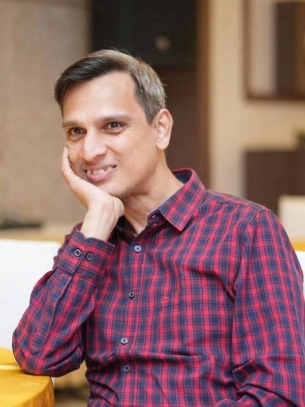 Man in a red checkered shirt resting his face on his hand with a gentle smile.