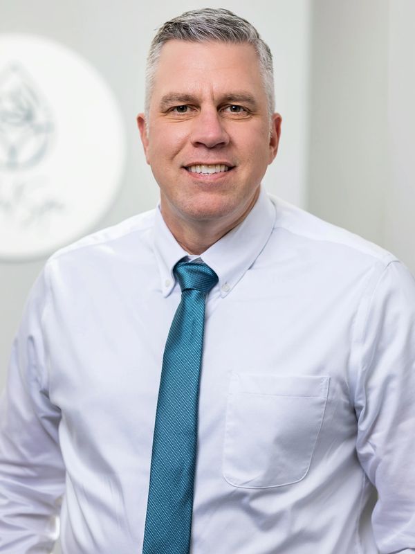 Smiling man in white shirt and blue tie posing indoors.