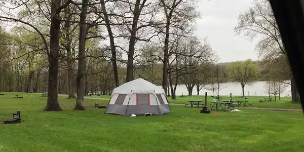 A tent set up in a grassy park near trees and a lake.