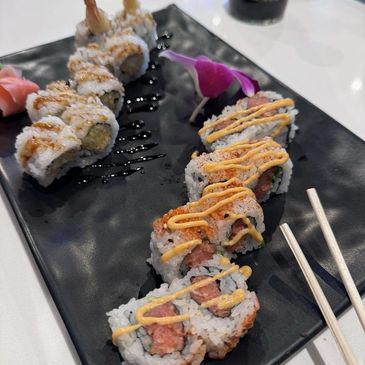 Sushi rolls with spicy mayo and eel sauce on a black plate.