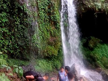 Group of men gathered near a lush green waterfall in a forest.
