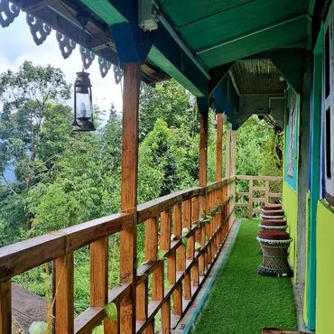 A wooden balcony with green artificial grass and stools overlooking lush trees.