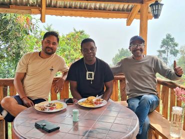 Three men enjoying a meal together on a wooden patio with nature around.