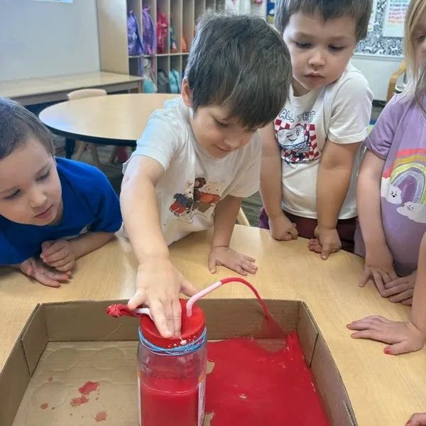 Children exploring a red liquid experiment in a classroom.