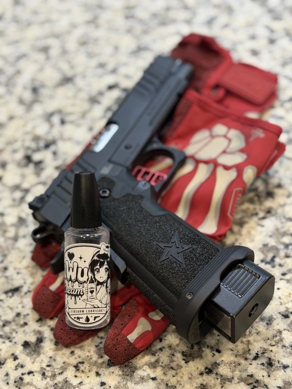 Black handgun with red gloves and gun lubricant bottle on granite surface.