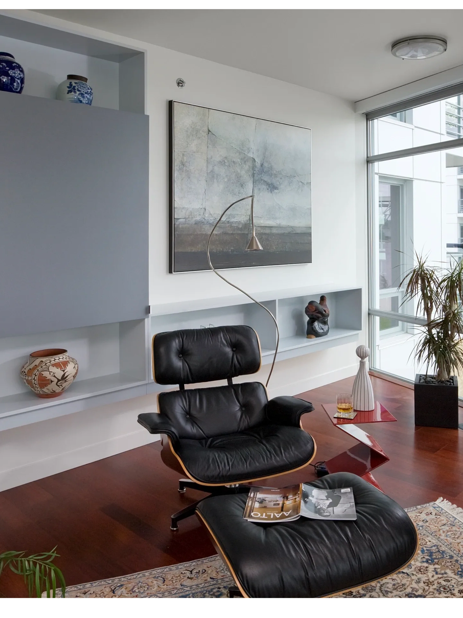 Eames lounge chair in front of a wall hung credenza and large piece of art.