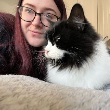 A woman with glasses and a black-and-white cat lying close together.