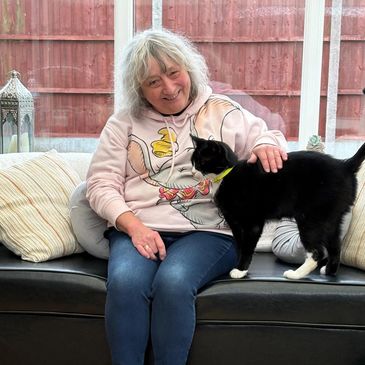 Woman in a pink hoodie smiling and petting a black and white cat on a couch.