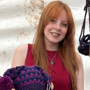 Young woman with long red hair smiling, holding a knitted hat.