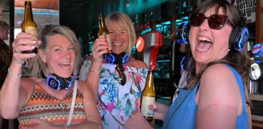 Three women joyfully celebrating with beer and headphones.