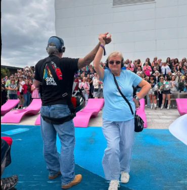 Two people dancing outdoors with a crowd in the background.