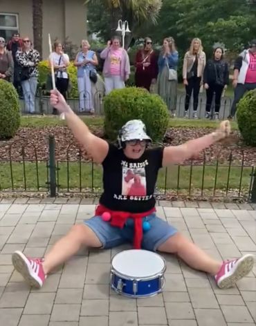 Person joyfully playing a drum in public.