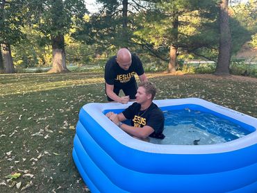 A baptism ceremony in a small inflatable pool outdoors.