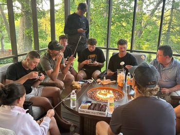 Group roasting marshmallows around a fire pit on a screened porch.