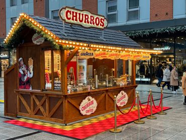 Festive churros and coffee stand with bright lights and holiday decorations.