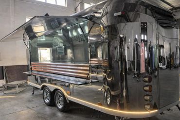 Shiny metallic food truck with an open service window inside a warehouse.