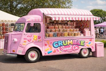 Pink candy truck with colorful sweets and striped awning outdoors.