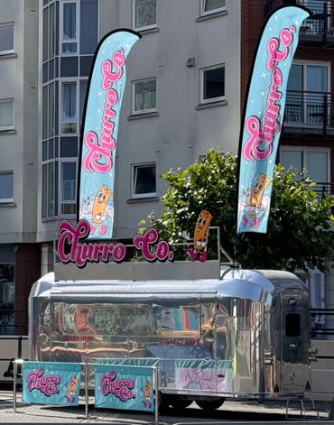 A shiny food truck with vibrant Churro Co. banners in an urban setting.