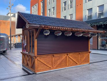 Closed wooden kiosk selling churros and coffee in an urban setting.