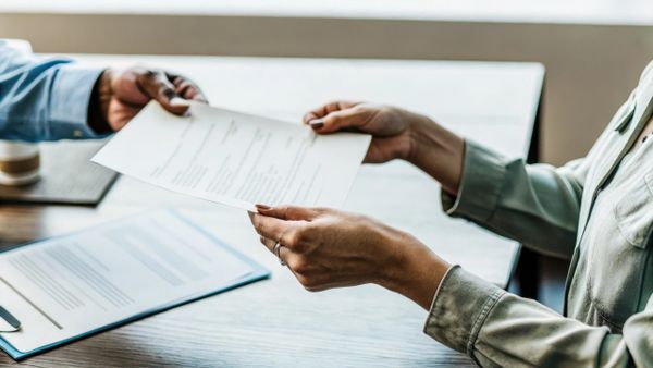 Two people exchanging documents across a table in a professional setting.