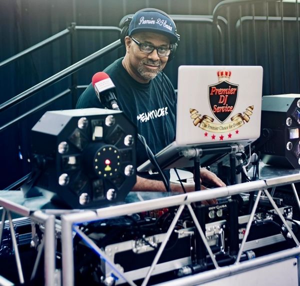 DJ wearing a Premier DJ Service cap and shirt, mixing music with professional equipment.