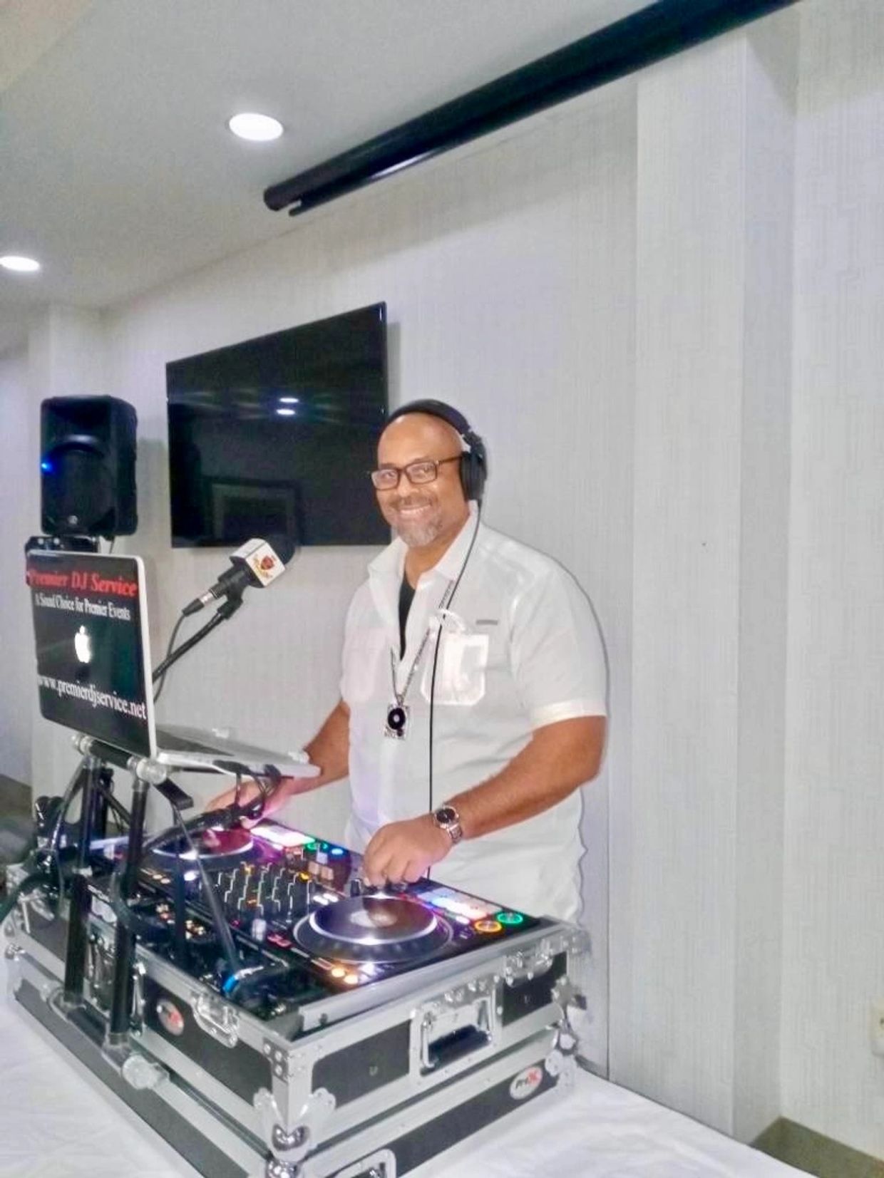 Smiling DJ wearing headphones, mixing music at a DJ booth with equipment and laptop.