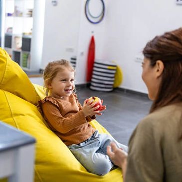 Child sitting on yellow bean bag holding a toy.