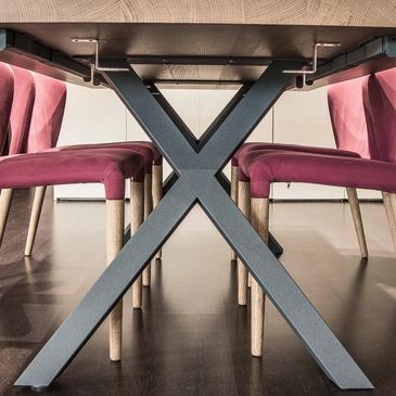 Modern dining table with pink cushioned chairs and X-shaped metal legs.