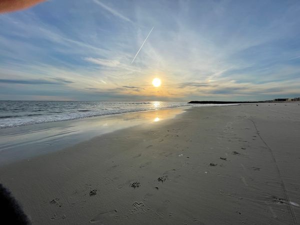 Sun setting over a calm beach with gentle waves and clear sky.
