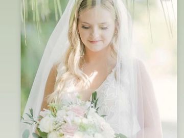 Bride in white dress holding bouquet with veil.