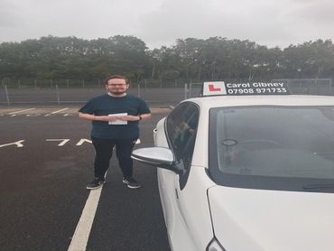Man proudly standing next to a white learner driver car holding a certificate.