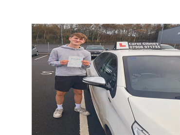 Young man proudly holding a driving test pass certificate beside a learner car.